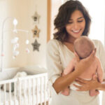 Young,Mother,Holding,Her,Baby,In,The,Bedroom