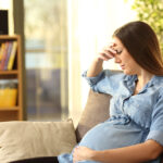 Worried,Pregnant,Woman,Sitting,On,A,Couch,In,The,Living