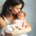 Mother,Kissing,Newborn,Son,At,Grey,Background.,Portrait,Of,Woman