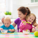 Mother,Feeding,Child,Fruit,And,Yoghurt.,Mom,Feeds,Kid,In