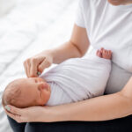 Swaddled,Newborn,Baby,Sleeping,In,Hands,Of,Her,Mother,At